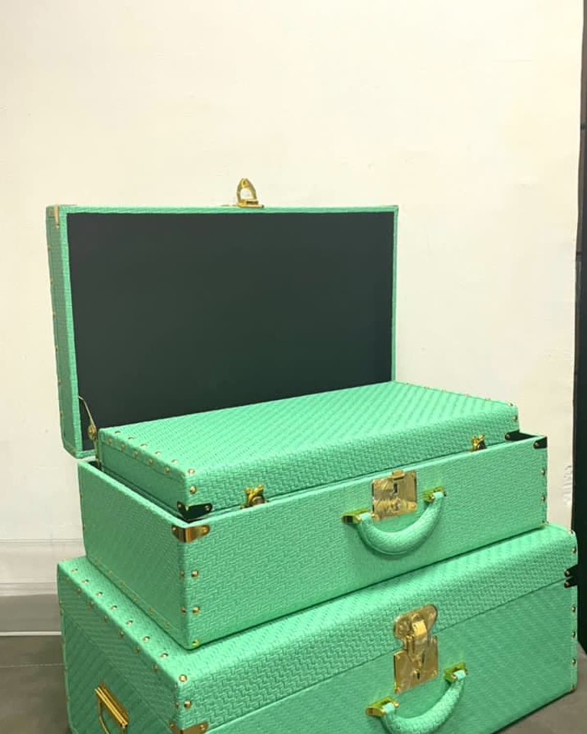 A pair of mint-green woven keepsake trunks with gold hardware